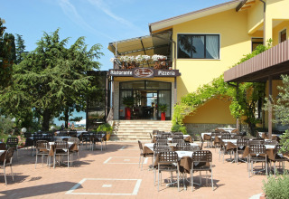 Udendørs restaurantområde på Camping Bella Italia feriepark i Veneto, Italien, med borde og stole under åben himmel.