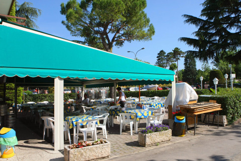 Outdoor dining area with green awning and plastic chairs at Camping Bella Italia, Veneto, Italy.