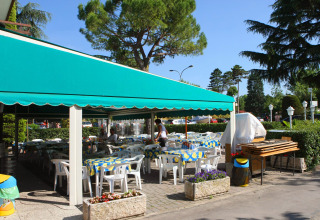 Outdoor dining area with green awning and plastic chairs at Camping Bella Italia, Veneto, Italy.
