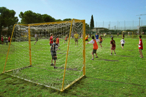 Niños juegan al fútbol en un campo de césped soleado en Camping Bella Italia, Veneto, Italia.