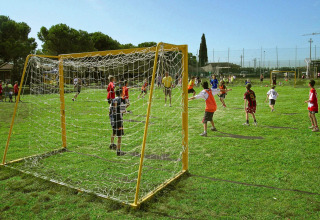 Bambini giocano a calcio su un campo erboso al sole al Camping Bella Italia, Veneto, Italia.