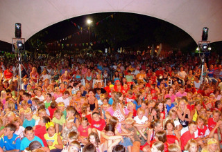 Grande gruppo di bambini e adulti riuniti sotto un tendone per una serata al Camping Bella Italia, Italia.