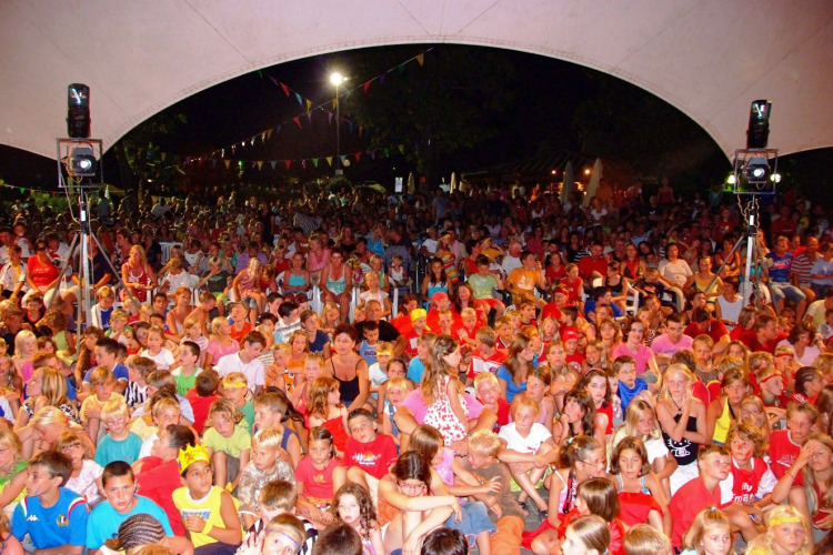 Large group of children and adults gathered under a tent for an evening event at Camping Bella Italia, Italy.