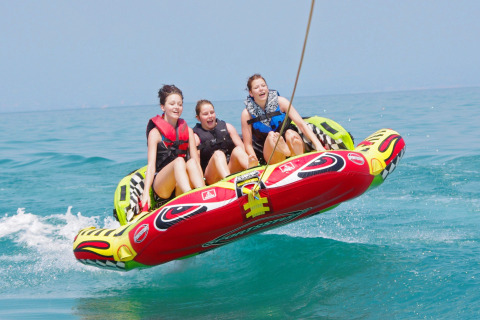Tres jóvenes disfrutan de un paseo en flotador inflable sobre el agua en Camping Bella Italia en Véneto, Italia.