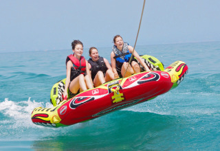 Tre ragazze si divertono su un gonfiabile trainato sull’acqua al Camping Bella Italia, Veneto, Italia.