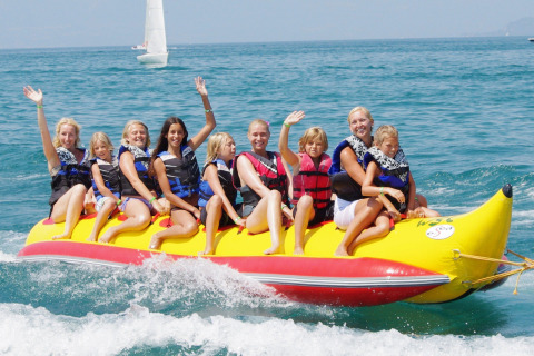 Grupo disfruta en una banana inflable amarilla en Camping Bella Italia, Veneto, Italia, entre risas y olas.