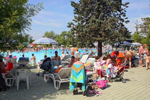 Familias descansando junto a la piscina concurrida en Camping Bella Italia, parque vacacional en Véneto, Italia.