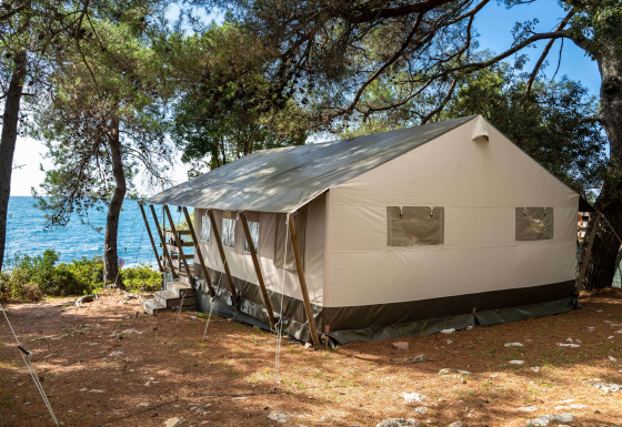 Tienda safari de lujo junto a pinos y vista al mar, ideal para una experiencia cómoda en la naturaleza.