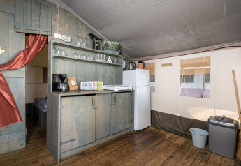 Kitchen area of a luxury safari tent with wooden flooring, shelves, fridge, and coffee maker in Croatia.