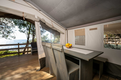 Vista interior de una tienda safari de lujo con mesa de comedor y vista al mar en Koversada Camping Resort, Croacia.