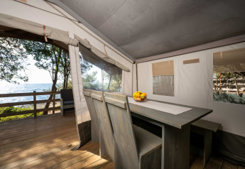 Vista interior de una tienda safari de lujo con mesa de comedor y vista al mar en Koversada Camping Resort, Croacia.