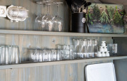 Kitchen shelves in a luxury safari tent with glasses, utensils, and a herb board on a wooden wall.
