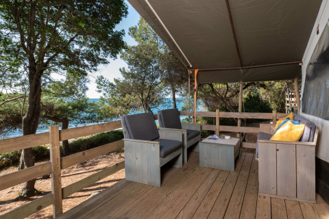 Terraza de madera con sofás, cojines y vista al mar en Safari Tent Luxury, Koversada Camping Resort, Croacia.