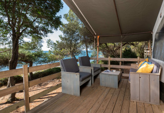 Terraza de madera con sofás, cojines y vista al mar en Safari Tent Luxury, Koversada Camping Resort, Croacia.