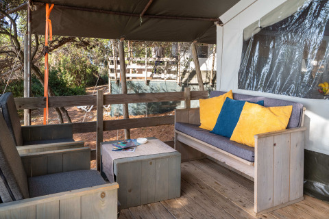 Zona de estar al aire libre con muebles de madera y cojines coloridos en Safari Tent Luxury del Koversada Camping Resort, Croacia.