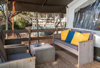 Zona de estar al aire libre con muebles de madera y cojines coloridos en Safari Tent Luxury del Koversada Camping Resort, Croacia.