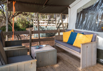 Zona de estar al aire libre con muebles de madera y cojines coloridos en Safari Tent Luxury del Koversada Camping Resort, Croacia.