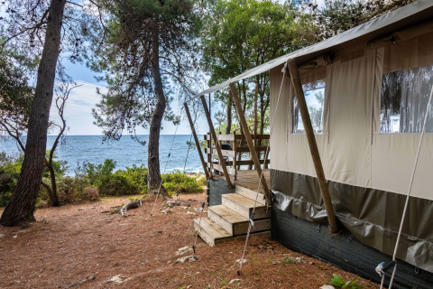 Luxus-Safarizelt am Meer im Koversada Camping Resort, Kroatien, mit Blick durch Kiefern auf das Wasser.