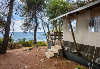 Luxus-Safarizelt am Meer im Koversada Camping Resort, Kroatien, mit Blick durch Kiefern auf das Wasser.