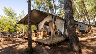 Safari telt Comfort med aircondition, placeret i en skov, med terrasse med havemøbler og køkken.