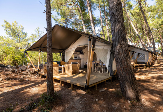 Safari telt Comfort med aircondition, placeret i en skov, med terrasse med havemøbler og køkken.