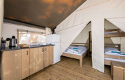 Interior view of a safari tent featuring a kitchenette, fridge, and sleeping area with beds and bunk bed.