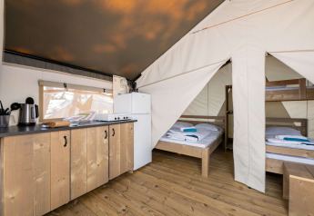 Interno di una tenda safari con angolo cottura, frigorifero e zona notte con letti e letto a castello.