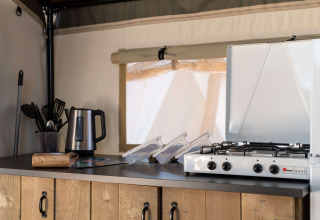 Zona de cocina en tienda safari con hervidor eléctrico, utensilios de cocina y estufa de gas sobre mostrador.