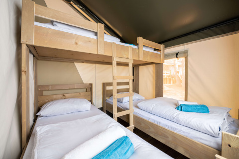 Zona de descanso en tienda safari, con una litera y dos camas individuales, ropa de cama blanca y toallas azules.
