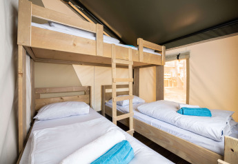 Slaapruimte in een safaritent met een stapelbed en twee eenpersoonsbedden, witte lakens en blauwe handdoeken.