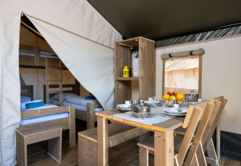 Interior of a safari tent featuring a wooden dining table, kitchenware, and wooden bunk beds in the back.