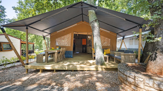 Tienda safari con instalaciones sanitarias, terraza de madera, comedor y zona de descanso bajo toldo.