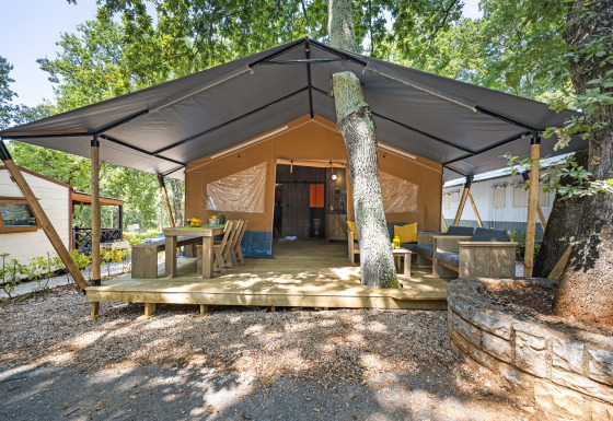 Safari tent met sanitair, houten terras, eethoek en lounge onder grote tentdoek en bomen.