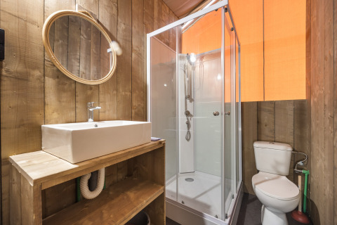 Badkamer met houten wanden, douche, toilet en wastafel in een safaritent, warme gezellige sfeer.