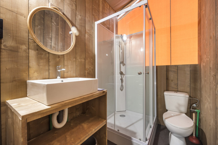 Badkamer met houten wanden, moderne douche, toilet en wastafel in een safaritent, knusse uitstraling.