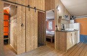 Interior de una tienda safari con paneles de madera, cocina pequeña, dormitorio y escalera al altillo.