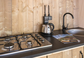 Encimera de cocina en tienda safari con cocina de gas, hervidor, grifo negro y folletos en Camping Aminess Maravea, Croacia.