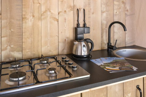 Encimera de cocina en tienda safari con cocina de gas, hervidor, grifo negro y folletos en Camping Aminess Maravea, Croacia.