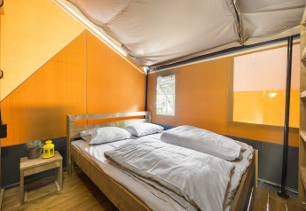 Vista interna di una tenda safari con pavimento in legno, letto matrimoniale, lenzuola bianche e tavolino.