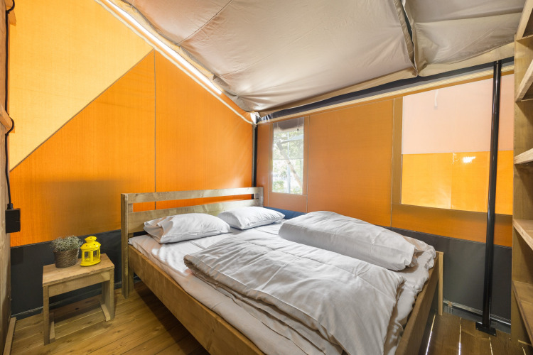 Interieur van een safaritent met houten vloer, tweepersoonsbed, witte lakens en klein bijzettafeltje.