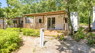 Moderne chalet Mobile home Funtana met houten terras, omgeven door bomen en groene natuur.