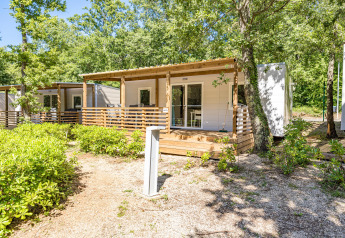 Chalet moderne nommé Mobile home Funtana avec terrasse en bois, entouré d’arbres et de végétation.