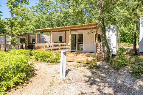 Casa mobile chiamata Mobile home Funtana con veranda in legno, immersa tra alberi e natura verde.