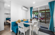 Moderne cabin met eethoek, blauwe gordijnen, witte tafel en uitzicht op terras met gekleurde hangmat.