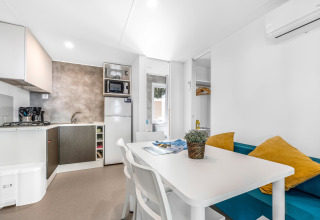 Moderne stacaravan-keuken en eethoek met witte tafel en blauwe bank in Camping Bijela Uvala, Kroatië.