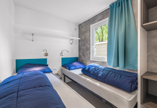 Habitación de cabaña luminosa y moderna con dos camas individuales, ropa de cama azul y cortinas azules.