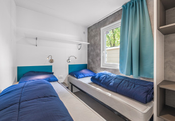 Bright and modern cabin room with two single beds, blue bedding, and a large window with blue curtains.