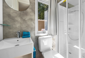 Salle de bain moderne de cabane avec douche, toilettes, fenêtre, miroir et lavabo. Serviettes bleues pliées.