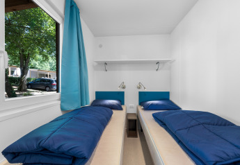 Twee eenpersoonsbedden met blauwe dekens in een helder vertrek van Mobile home Funtana, Camping Bijela Uvala.