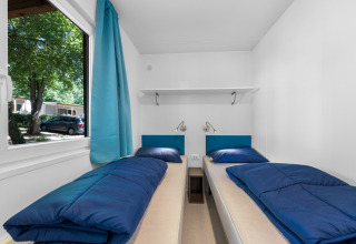 Twee eenpersoonsbedden met blauw beddengoed in een lichte kamer van Mobile home Funtana, Camping Bijela Uvala.